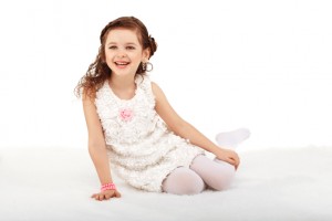 Portrait of a pretty little fun fashion girl sitting on a fluffy rug on the floor and having fun against white background